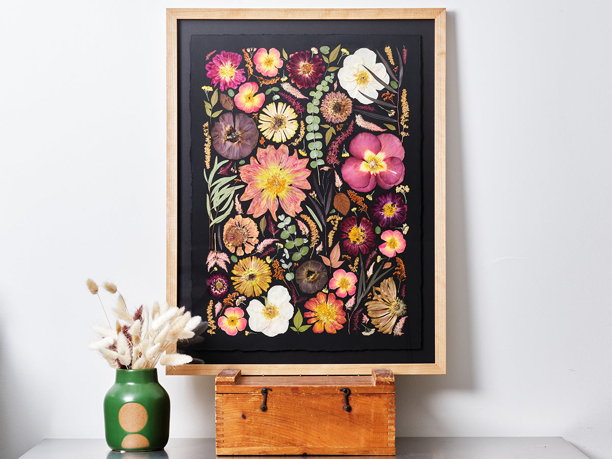 Purple, pink, and white flowers that are pressed and dried and then framed in wood.