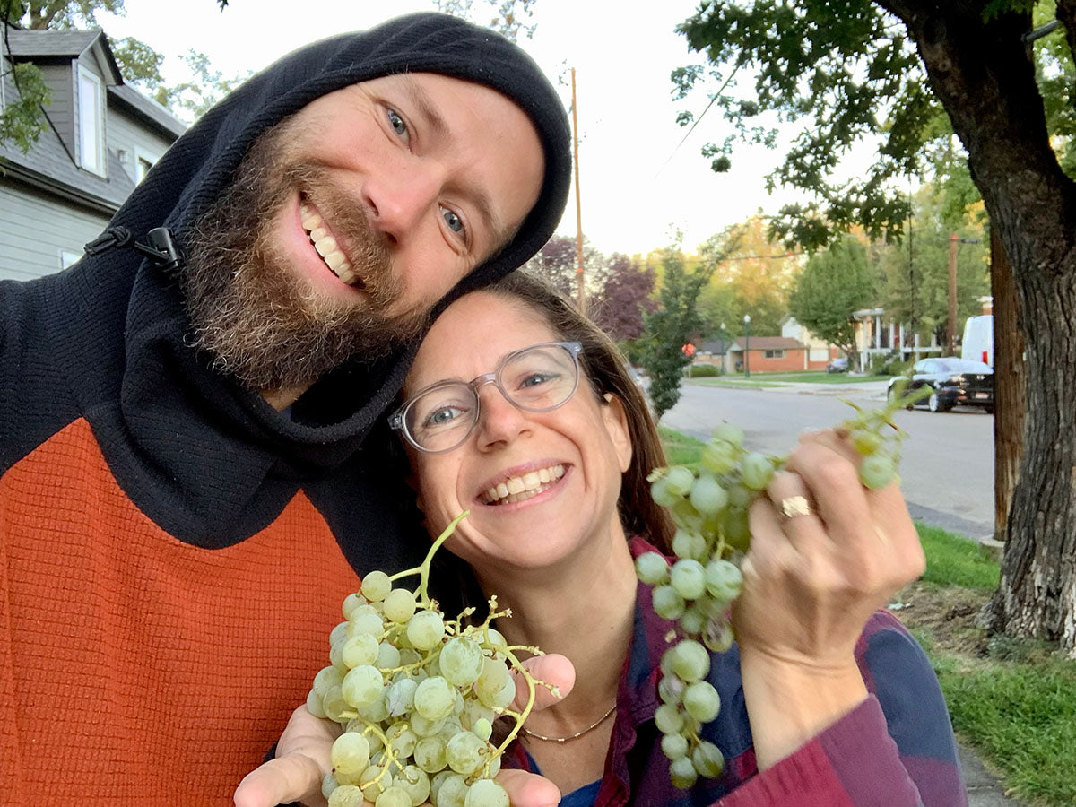Keith and Rachel holding a bunch of grapes, owners of Flower Press Studio